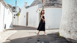 Frau im schwarzen Kleid und weißen Korkpantoletten in einer Gasse in Italien. Könnte vom Look aber auch Griechenland sein. Schön so oder so