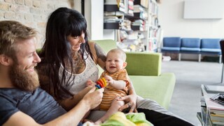 Mann, Frau, Baby, alle lachen und spielen auf dem Sofa