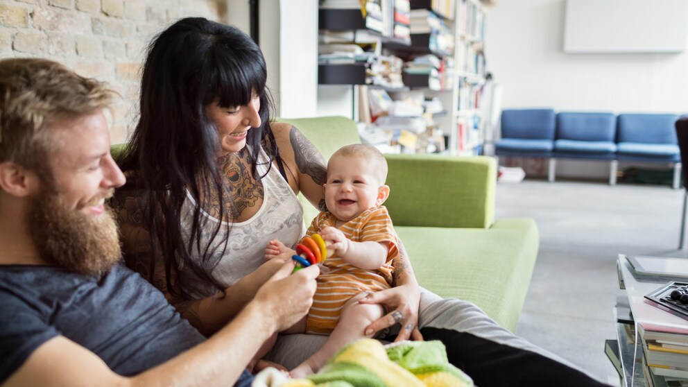 Mann, Frau, Baby, alle lachen und spielen auf dem Sofa