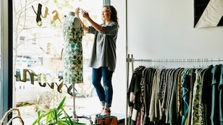 Frau zieht einer Puppe im Schaufenster ein Kleid an