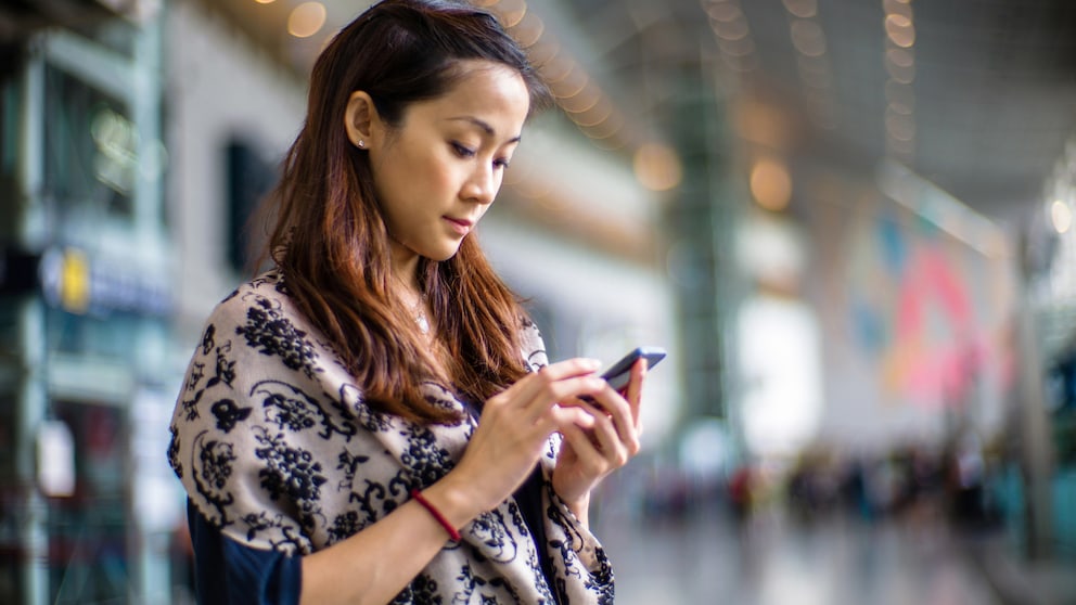 Frau mit Handy am Bahnhof