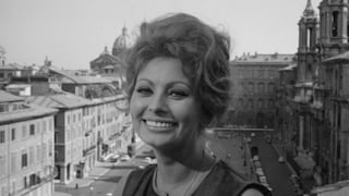 Sophia Loren lächelt sehr süß in die Kamera. Hinter ihr eine italienische Stadtkulisse