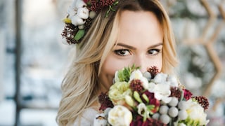 Frau mit Strauß und Brautkleid. Sie lächelt verschmitzt und wirkt, als würde sie ihren Namen nach der Hochzeit behalten. Bitte nicht persönlich nehmen, natürlich können Frauen, die ihren Namen behalten, aussehen, wie sie wollen. Es ist ja auch nur ein Beispielbild