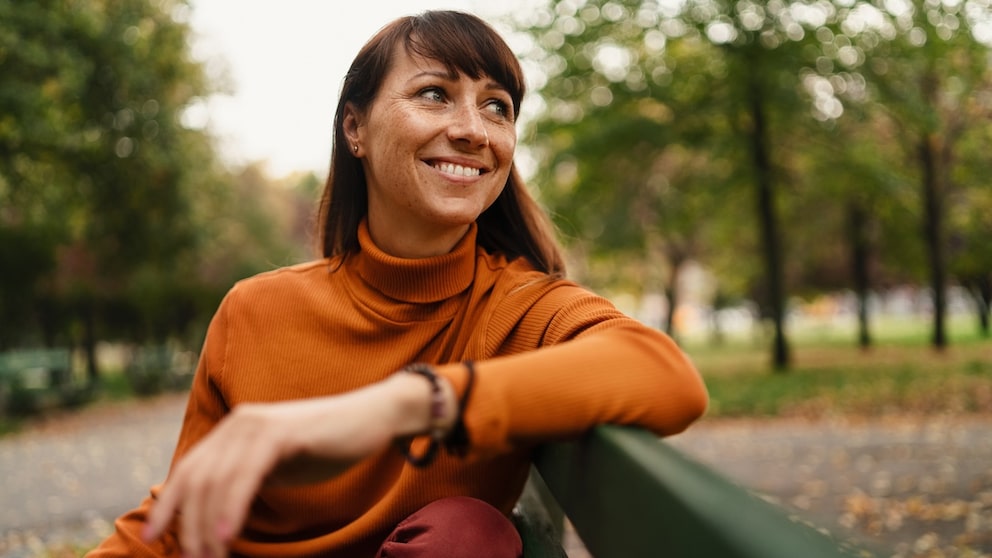 Frau sitzt glücklich lachend auf Bank, bestimmt hat sie Thymian gegen Menstruationsbeschwerden genommen