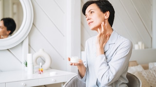 Frau schmiert sich Creme ins Gesicht