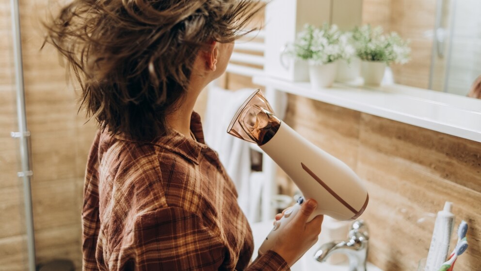 Frau mit Föhn in der Hand trocknet ihre Haare