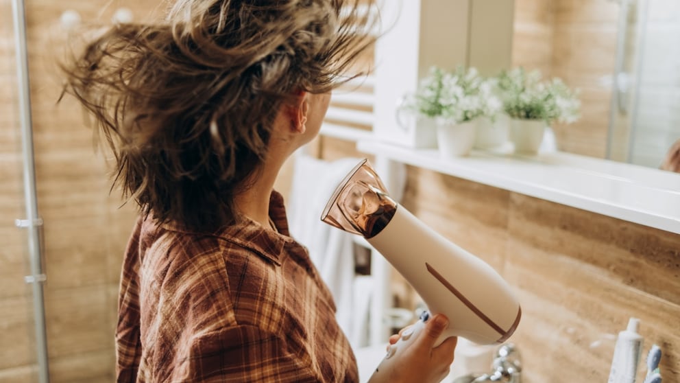 Frau mit Föhn in der Hand trocknet ihre Haare