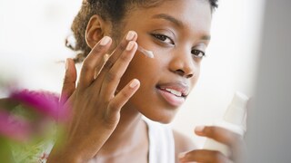 Frau schmiert sich Creme ins Gesicht
