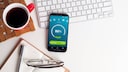 Smartphone liegt auf dem Tisch neben einer Tastatur und einer Tasse Kaffee