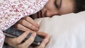 Frau liegt im Bett mit ihrem Handy in der Hand