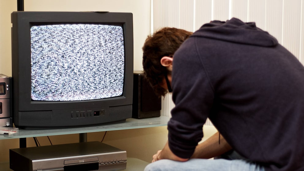 Mann sitzt mit gesenktem Kopf vor dem Fernseher