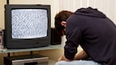 Mann sitzt mit gesenktem Kopf vor dem Fernseher