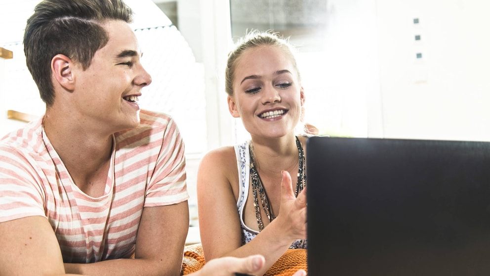Junge und Mädchen lachen vor einem Laptop