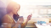 Frau sitzt im Zug und hält ein Handy in der Hand