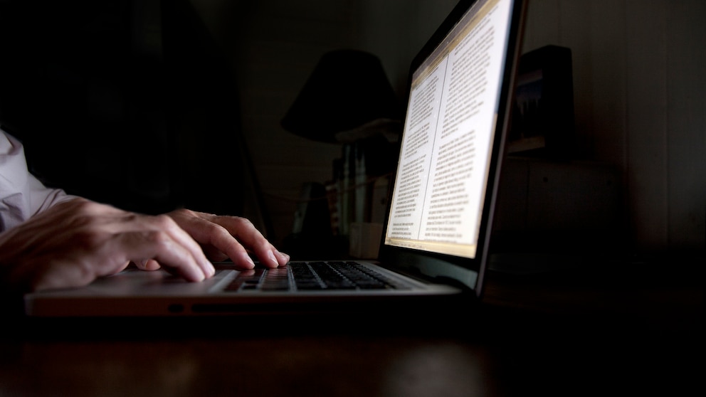 Laptop im Dunkeln mit Händen, die tippen