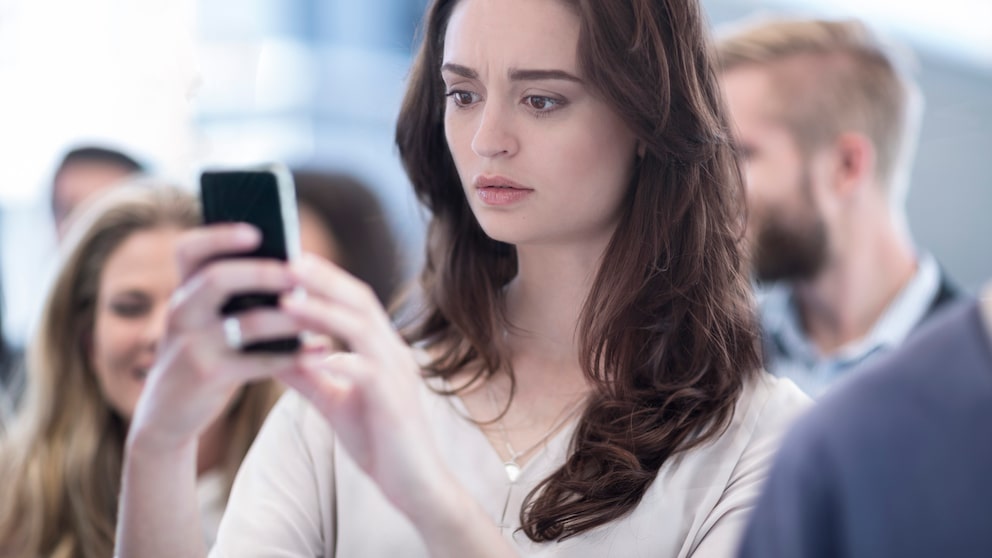 Frau schaut verunsichert auf das Handy.