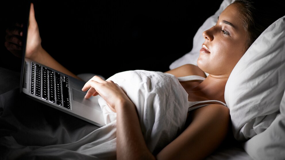 Frau liegt im Bett mit Laptop