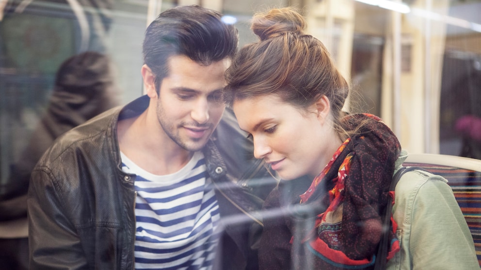 Pärchen steht in der Bahn uns schaut auf ein Smartphone