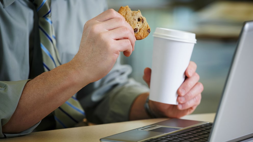 Mann mit Keks und Kaffee vor dem Laptop