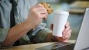 Mann mit Keks und Kaffee vor dem Laptop