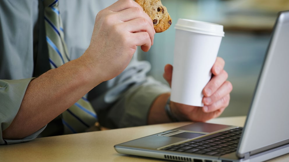 Mann mit Keks und Kaffee vor dem Laptop