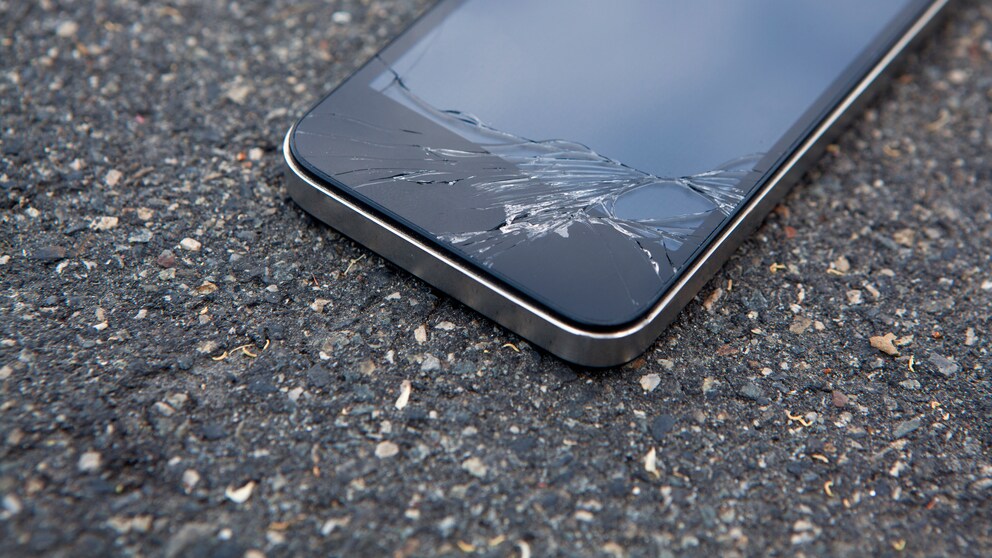 Smartphone mit gesprungenem Display auf Asphalt
