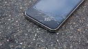 Smartphone mit gesprungenem Display auf Asphalt