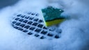 A computer keyboard being cleaned in soap suds and water with a yellow kitchen sponge.
