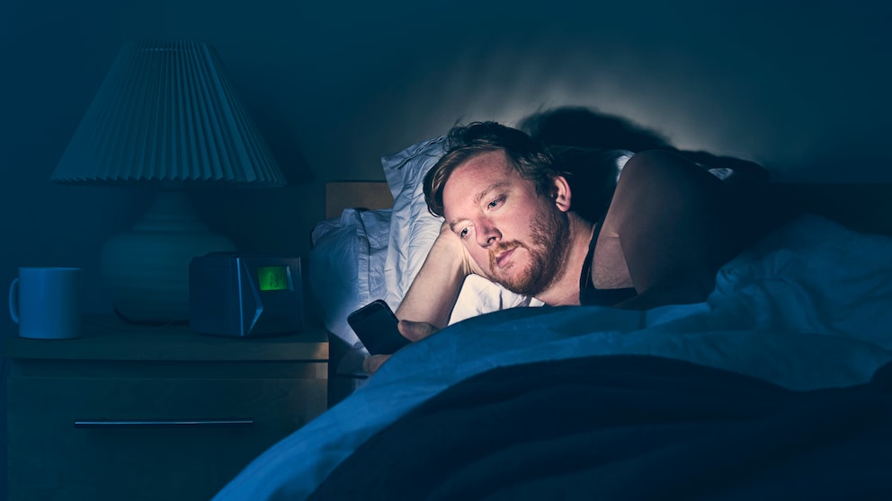 Mann liegt im Bett schaut auf sein Handy