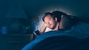 Mann liegt im Bett schaut auf sein Handy