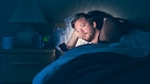 Mann liegt im Bett schaut auf sein Handy