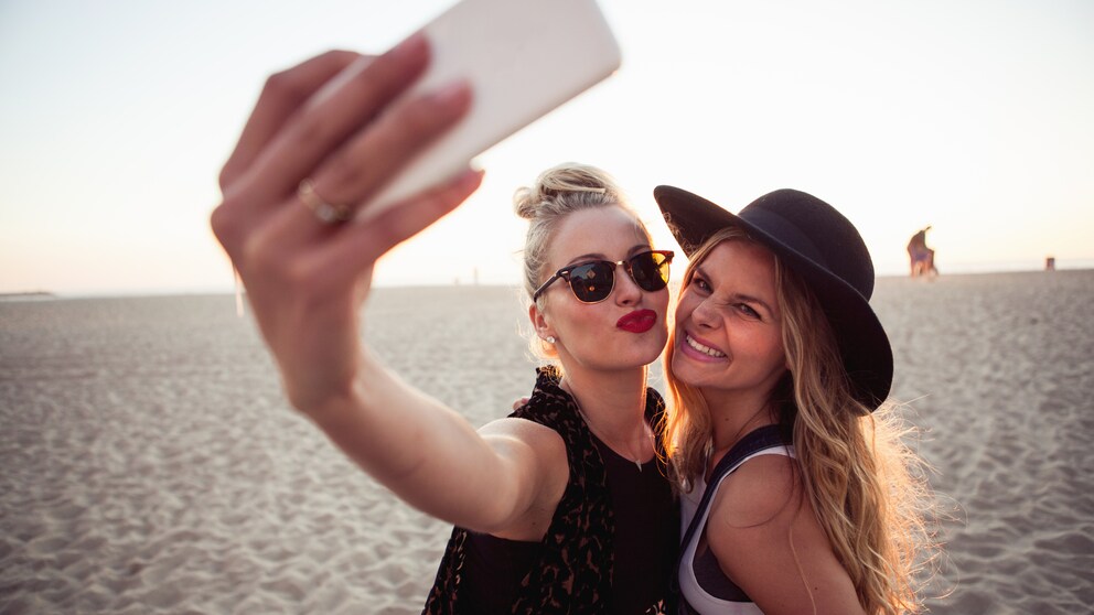 Zwei frauen stehen am Strand und machen mit ihrem Smartphone ein Selfie