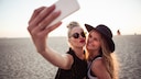 Zwei frauen stehen am Strand und machen mit ihrem Smartphone ein Selfie