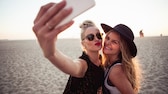 Zwei frauen stehen am Strand und machen mit ihrem Smartphone ein Selfie