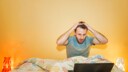mann sitzt im Bett mit seinem Laptop und guckt geschockt