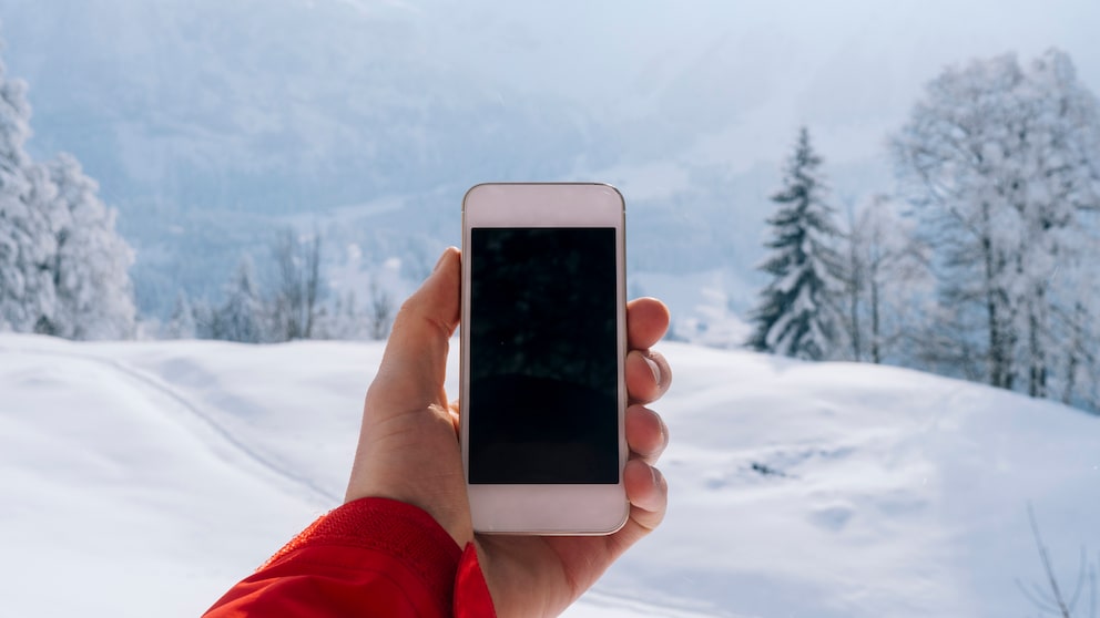 Mann hält Smartphone vor Winterlandschaft