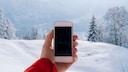 Mann hält Smartphone vor Winterlandschaft