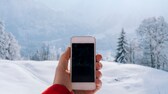 Mann hält Smartphone vor Winterlandschaft