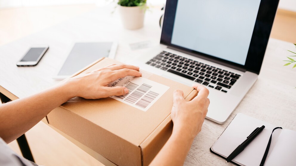 Frau mit Laptop und Paket auf Schreibtisch