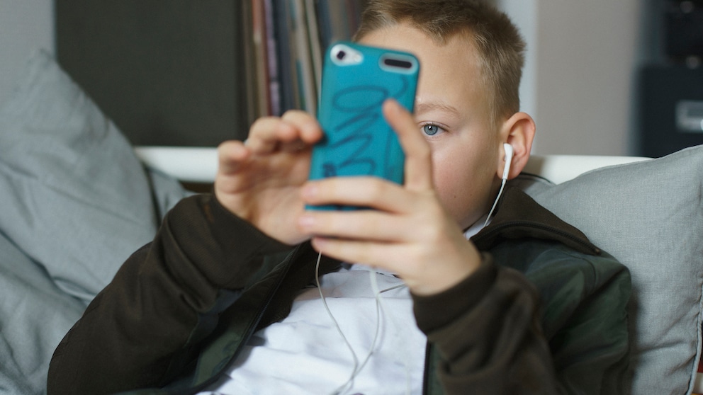 Junge liegt auf dem Bett und hat ein Handy in der Hand und hört Musik