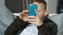 Junge liegt auf dem Bett und hat ein Handy in der Hand und hört Musik