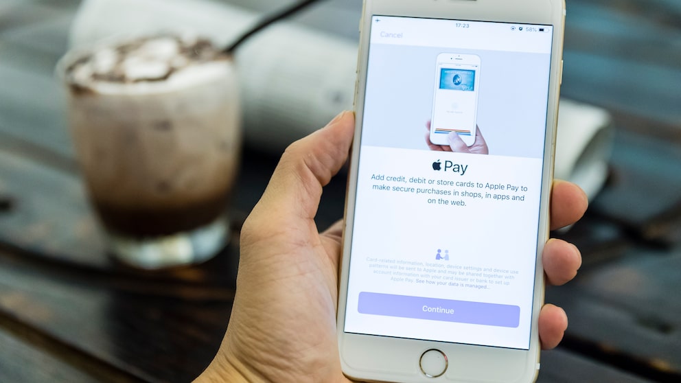 Hand hält Handy auf dem Apple Pay zu sehen ist