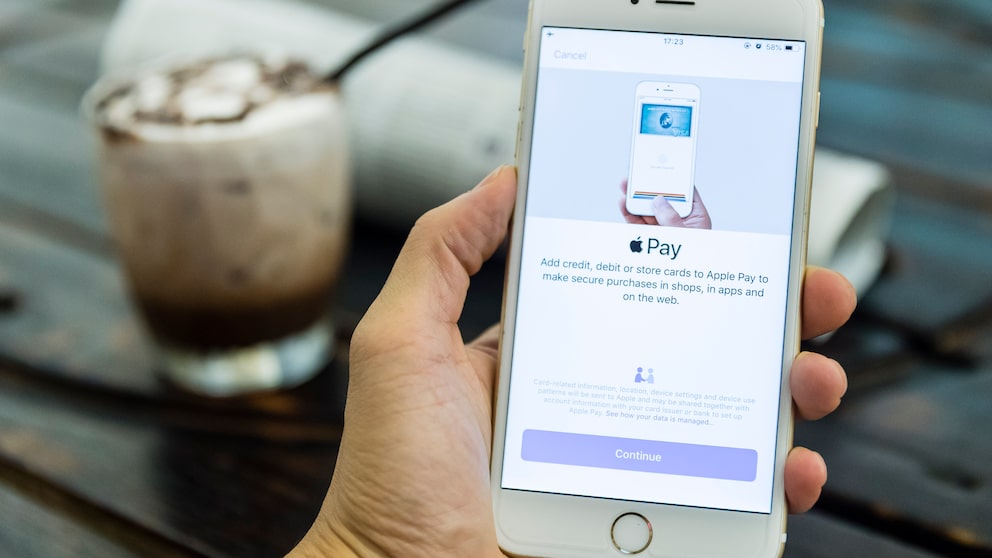 Hand hält Handy auf dem Apple Pay zu sehen ist