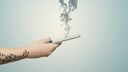 Eine Hand hält ein rauchendes Smartphone fest