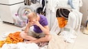 Mann sitzt auf Wäschhaufen neben Waschmaschine