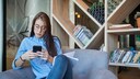 Frau sitzt auf einer Couch mit einem schwarzen Handy in der Hand