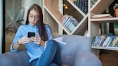 Frau sitzt auf einer Couch mit einem schwarzen Handy in der Hand