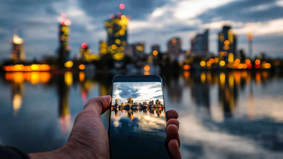 Mann hält Smartphone in der Hand, auf dem Display sieht man die Skyline von Wien
