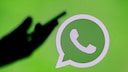 Hand hält Smartphone vor WhatsApp-Logo-Hintergrund