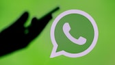 Hand hält Smartphone vor WhatsApp-Logo-Hintergrund